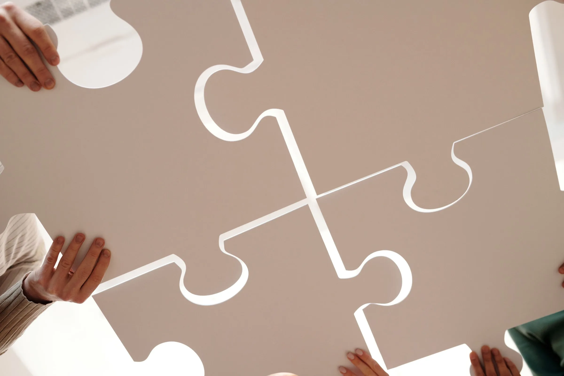 Several hands fitting large white puzzle pieces together
